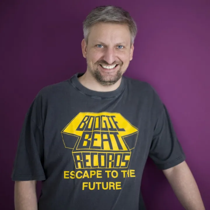 Dash smiling in a Boogie Beat Records T-shirt in front of a purple wall
